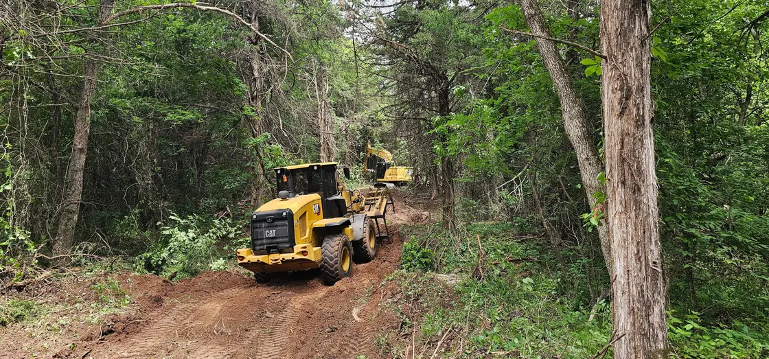Wheel loader and excavator cutting a new access road through dense timber on Oklahoma acreage