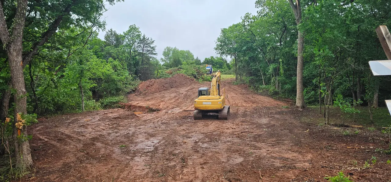 Excavator opening a wide access road cut through wooded acreage in Oklahoma