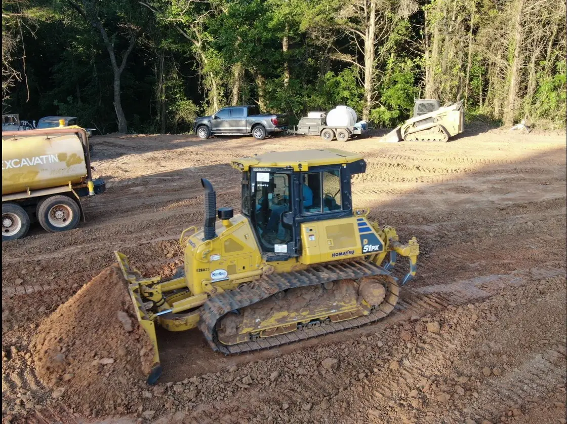 Dozer grading a building pad with a water truck and track loader staged behind it in Oklahoma