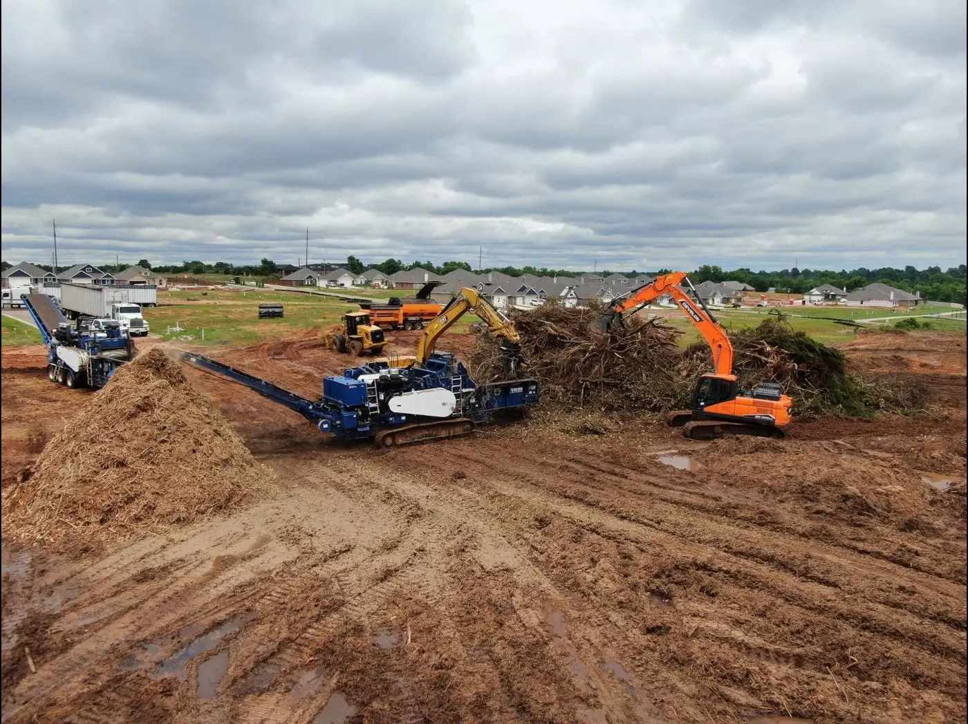 Grinder and excavators processing cleared brush on a development site beside a subdivision near Oklahoma City