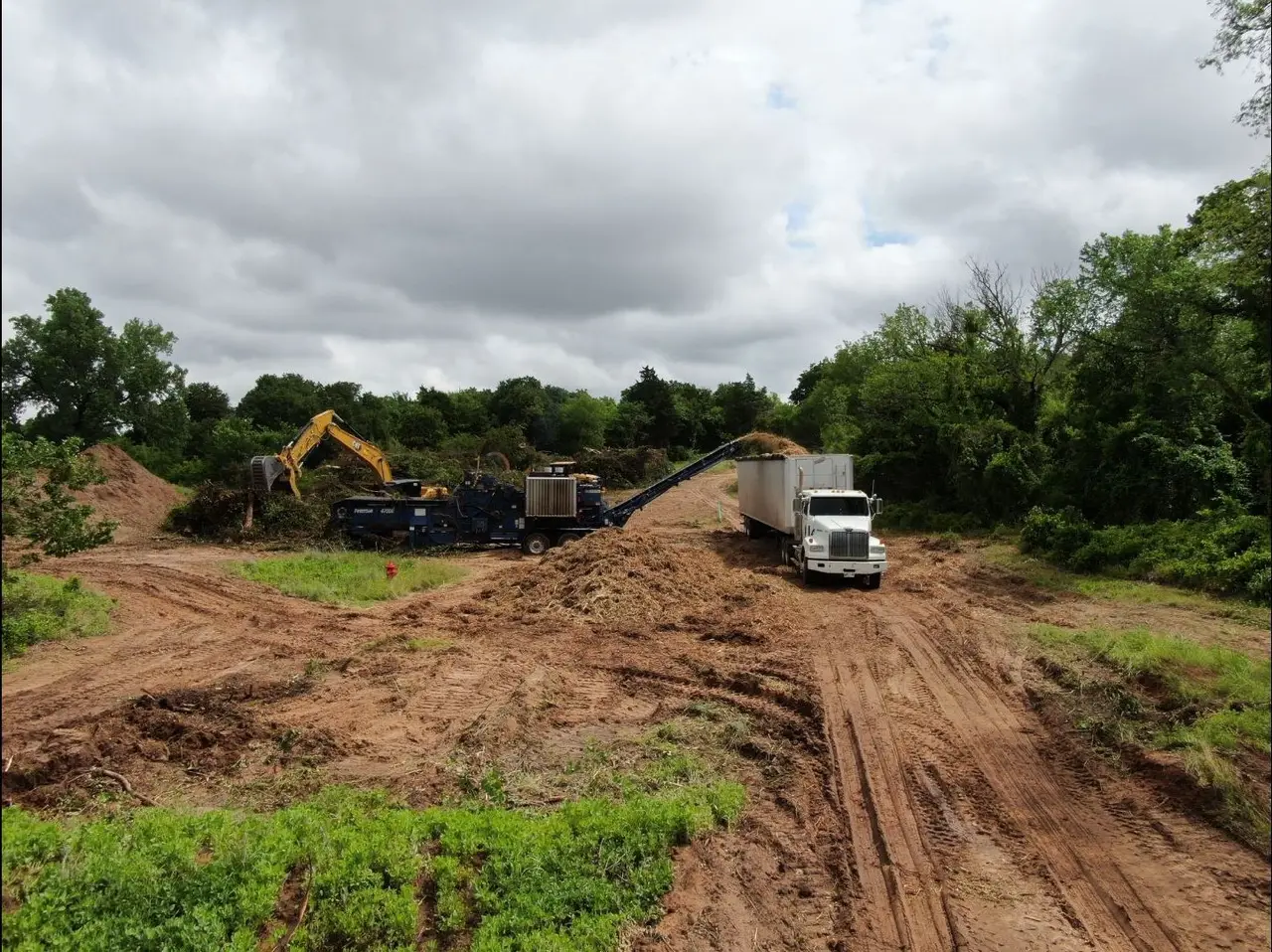 Excavator and grinder loading ground brush into a semi trailer on a cleared Oklahoma corridor